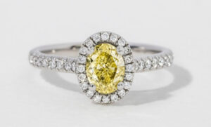 A silver ring featuring an oval yellow diamond surrounded by smaller clear diamonds on its band and setting.