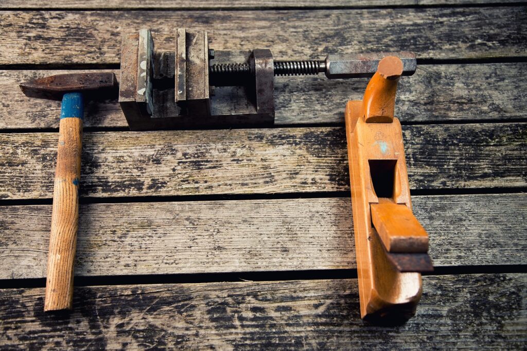 **Alt text:** A hammer, a vise, and a wooden hand plane are laid out on a rustic wooden surface.