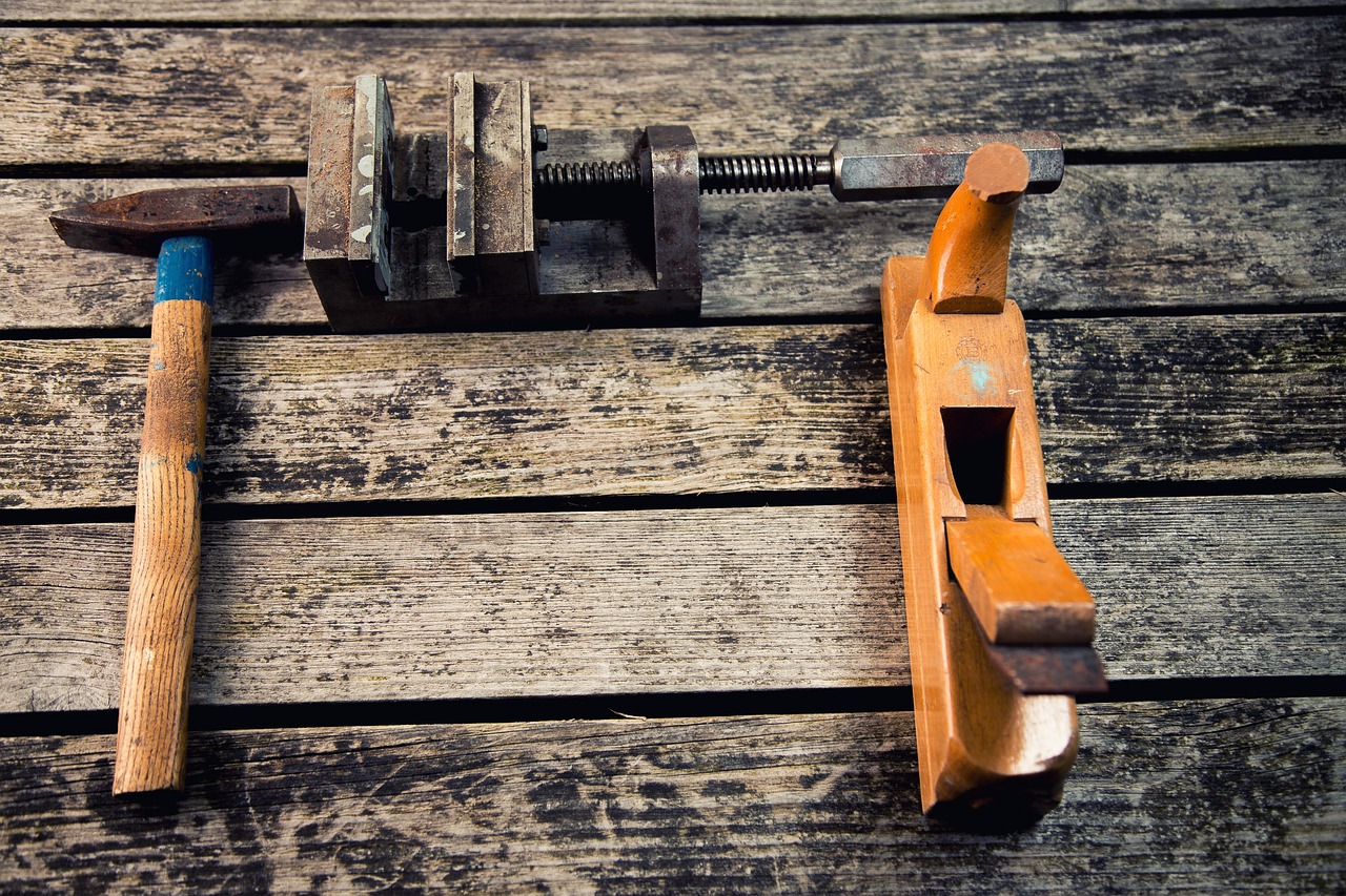 **Alt text:** A hammer, a vise, and a wooden hand plane are laid out on a rustic wooden surface.