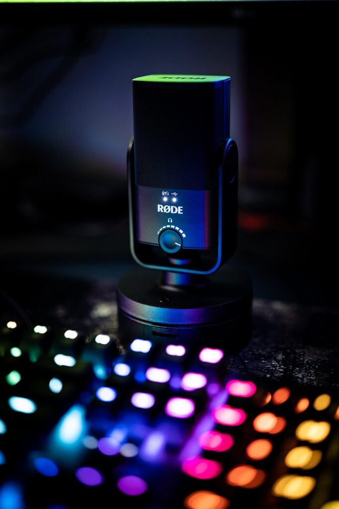 A dark studio setup featuring a RODE microphone illuminated by colorful lights from a nearby keyboard.