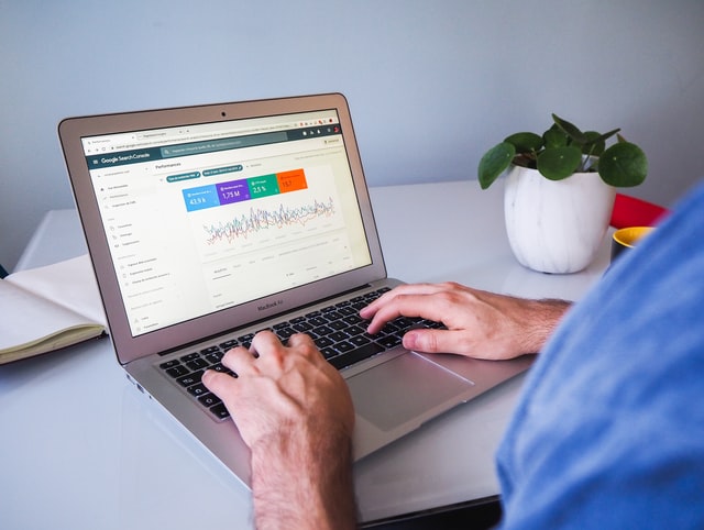 A person using a laptop displaying Google Search Console with performance data, seated at a desk with a small potted plant.