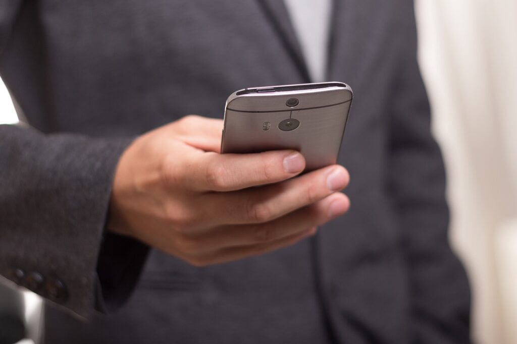 **Alt text:** A person in a suit jacket holds a smartphone in their hand.