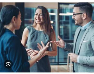 **Alt Text:** Three people are engaged in a lively conversation in an office setting, with one woman smiling broadly.