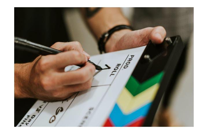 **Alt Text:** A person writes on a film clapperboard with a pen, holding it in one hand.