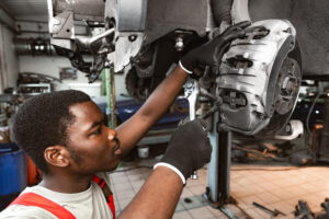 **Alt Text:** A mechanic is working on a car brake system using a wrench in an auto repair shop.