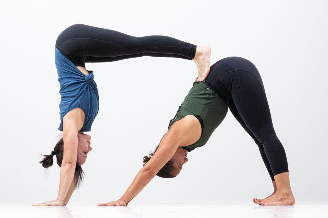 Two people are performing an acroyoga pose, with one balancing upside-down on the back of the other.