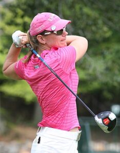 Alt text: A golfer in a pink outfit finishes a swing with a driver on a golf course.