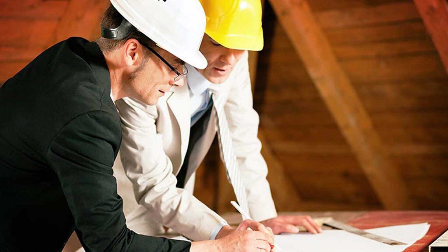 **Alt text:** Two men wearing hard hats and suits are reviewing architectural plans on a table.