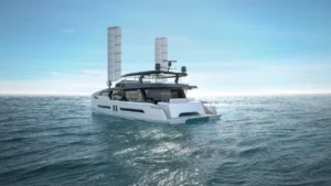 Alt text: A sleek, modern yacht with tall vertical structures cruising on a calm ocean under a clear blue sky.