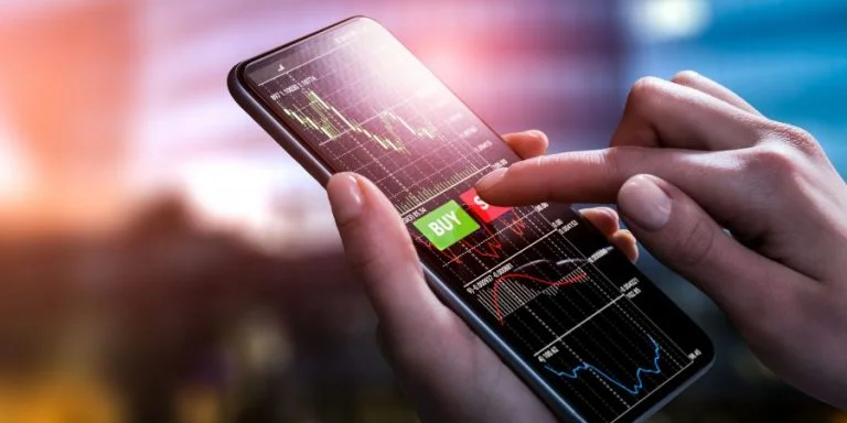 A person holding a smartphone with a trading app displaying financial charts and a "Buy" button on the screen.