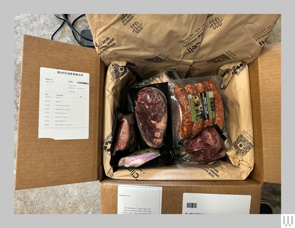 An open cardboard box containing vacuum-sealed packages of various meats with a packing list attached to the lid.