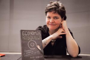 Alt text: A person smiling and resting their chin on their hand next to the book "Economía Rosquilla" on a table.