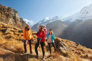 **Alt Text:** Three people are hiking in a mountainous area with snow-capped peaks in the background.