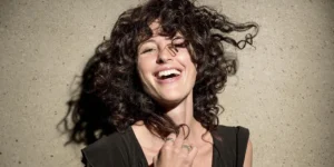 **Alt Text:** A woman with curly hair laughs joyfully against a stone wall.