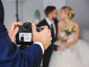 **Alt text:** A photographer captures a blurred image of a bride and groom in focus on the camera's display screen.