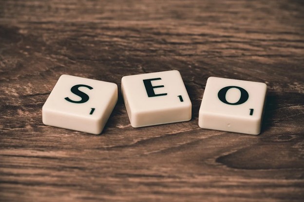 **Alt Text:** Three Scrabble tiles on a wooden surface spell out the word "SEO."