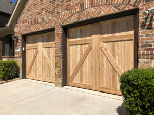 **Alt text:** A red brick house features two wooden garage doors with a diagonal cross design, set beneath matching brick arches.