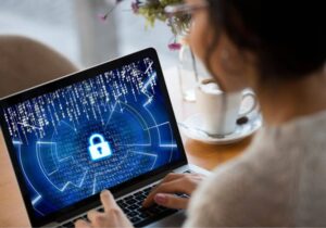 **Alt text:** A person works on a laptop displaying a digital padlock icon and binary code, symbolizing cybersecurity.