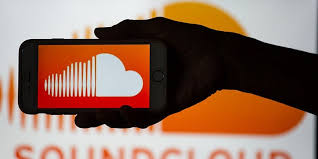 **Alt text:** A silhouette of a hand holding a smartphone displaying the SoundCloud logo with the same logo blurred in the background.