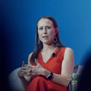 A woman in a red dress is speaking while seated against a blue background.