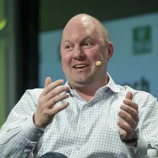 Alt text: A man in a checkered shirt speaks animatedly, gesturing with his hands and wearing an earpiece microphone.