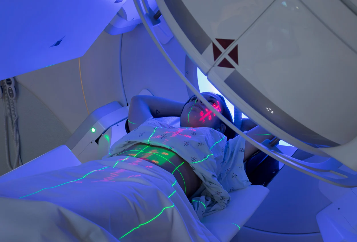 A person lies on a table inside a medical imaging machine, with laser lines projected onto their body.