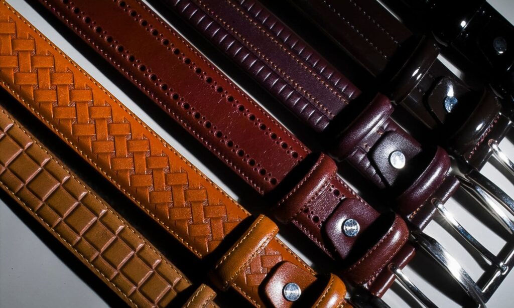 A collection of leather belts in various colors and textures laid out side by side.