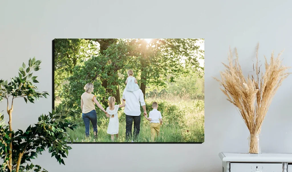 **Alt text:** A wall-mounted photograph of a family walking through a sunlit field with trees, surrounded by home decor including plants and pampas grass.