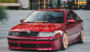 Alt text: A shiny red car with gold wheels parked in front of stairs.