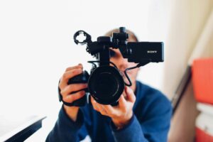 **Alt Text:** A cameraman holding a Sony video camera close to the lens, focusing on the camera from a front view.