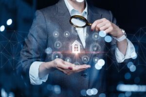 Alt text: A person holding a magnifying glass examines glowing digital icons surrounding a small house graphic.