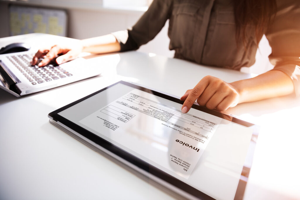 **Alt Text:** A person is using a tablet to view an invoice while typing on a computer keyboard.