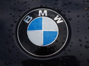 **Alt Text:** Close-up of a BMW logo on a black surface with water droplets.