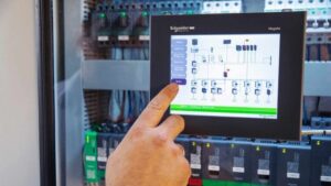 Alt text: A person is using a Schneider Electric control panel screen in front of a circuit board.