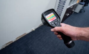 Alt text: A person holds a thermal imaging device displaying a heat map towards a wall.