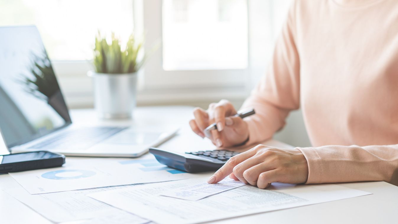 ALT Text: A person working at a desk with a laptop, calculator, and documents.
