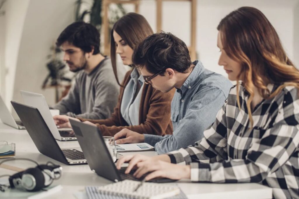 **Alt text:** Four people sitting at a table, focused on their laptops and documents.