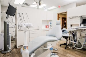 **Alt text:** A modern dental office with a dentist chair, medical equipment, and a computer workstation.
