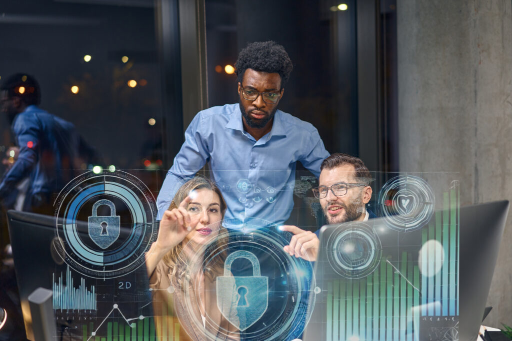 Alt text: Three people in an office setting are analyzing digital security graphics displayed on a transparent screen.